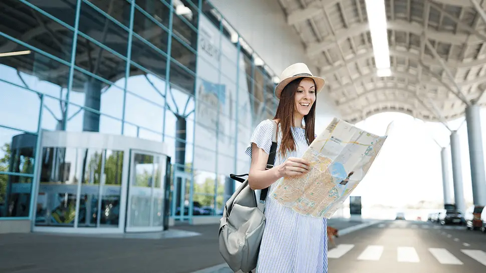young smiling traveler tourist woman with backpack holding paper map international airport best credit card to travel for free